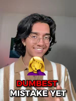 A smiling young man with dark hair and glasses is the focal point, set against a muted background. He's wearing a striped shirt with a brown collar, and a large emoji of a facepalm covers the area of his chest and shoulders. Bold, red text at the bottom reads "DUMBEST MISTAKE YET".