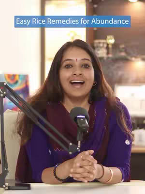 A woman with long brown hair is in front of a microphone, with text overlay at top that says "Easy Rice Remedies for Abundance". She is smiling. She is wearing a purple top with a dark burgundy scarf, and bracelets are visible on her wrist. The background shows a room setting, suggesting a recording studio.