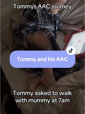 A person in pajamas is holding a tablet with an AAC (Augmentative and Alternative Communication) app while lying on a bed. The image uses a soft, muted color palette, possibly in a bedroom setting, with natural lighting.