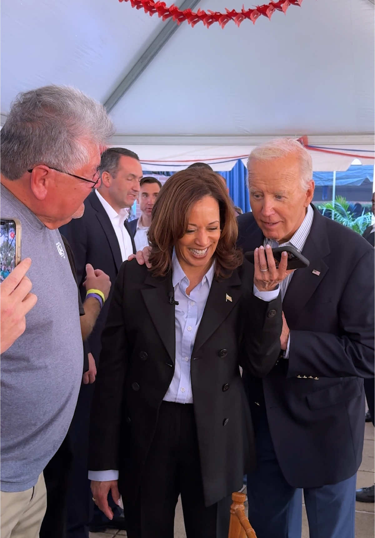 The cover image features a medium shot of Vice President Kamala Harris smiling while looking at a smartphone held by President Joe Biden. Both are surrounded by other individuals in the background, suggesting a public event. The composition is well-lit, indoors, with a partial view of an outdoor setting visible in the background.