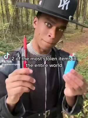 A person stands in front of a green background, wearing a black hat with a white logo, a black jacket, and is holding a red pen in one hand and a blue lighter in the other hand. Text overlayed on the image states '2 of the most stolen items in the entire world'.