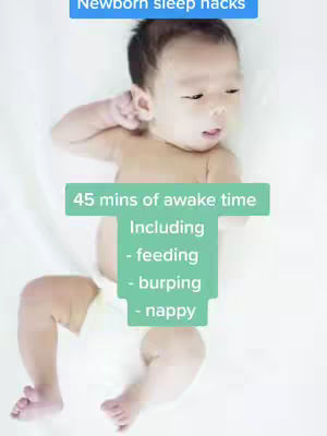 A baby lies on a white surface, likely a bed or changing table, with a few text overlays. The baby is lying down and looking toward the right of the frame. The image is dominated by white, suggesting a clean and simple composition.