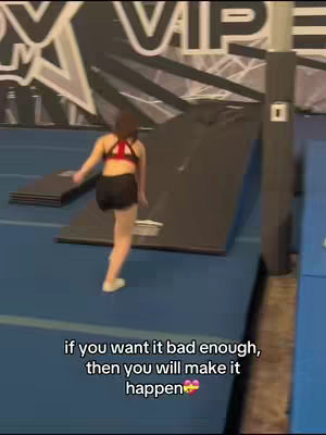 A young woman, seen from the rear, is walking towards an inclined training platform in a gym. She is wearing a sports bra and shorts. Below, overlaid text reads "if you want it bad enough, then you will make it happen." The background is a gym setting with branding on the wall.