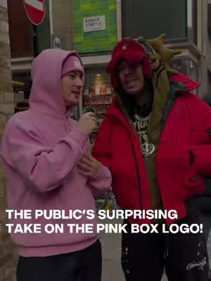 Two men are standing on a city street, one in a pink hoodie and the other in a red jacket. The hook text is at the bottom in white letters.