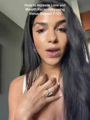A woman with long, dark hair is centered in the frame. She is wearing a white top and a silver ring. The image has text overlayed on the top of her head.