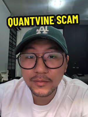 A selfie-style video cover image featuring a man with glasses and a baseball cap. Text overlay reads "QUANTVINE SCAM". The man has a neutral expression, making the image seem urgent.