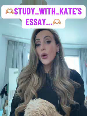 A woman with long blonde hair is centered in the frame, looking directly at the camera with a slightly open mouth. Above her, a text overlay reads "STUDY_WITH_KATE'S ESSAY..." in a light-colored box. The background is a blurred interior with visible curtains and a hint of a light fixture.
