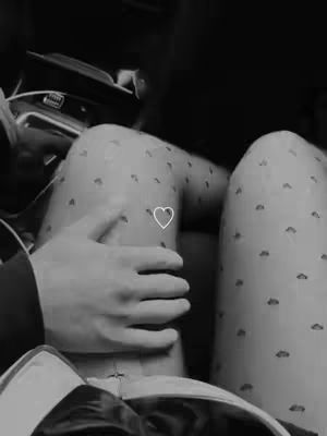 Black and white image showing a person embracing another, emphasizing the legs. The focus is on the lower body, with two sets of legs visible. One pair is covered in a pattern of small, dark shapes, and the other has someone's hand resting on it. A heart symbol is overlaid. The composition is intimate and uses grayscale tones.
