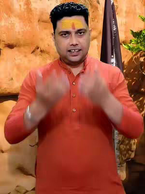 A man with a yellow mark on his forehead is shown in front of a textured background in an orange shirt. His hands are up near his face, as if he is speaking