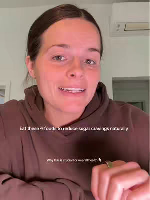 The cover image shows a woman in a close-up shot, likely in a home setting, as suggested by the light-colored wall and air conditioning unit in the background. She is wearing a brown hoodie, and her expression is engaged and direct, with her mouth slightly open as if speaking. Text overlays include the hook which says "Eat these 4 foods to reduce sugar cravings naturally" and then another overlay with slightly smaller text reads, "Why this is crucial for overall health". The lighting is soft and natural, and the overall composition is simple, focusing on the woman's face and the message she is conveying.