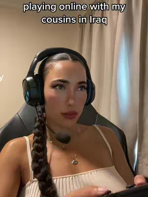 A woman with long, dark hair in a braid sits in a gaming chair, wearing a headset and holding a game controller. Text on the image reads, "playing online with my cousins in Iraq."
