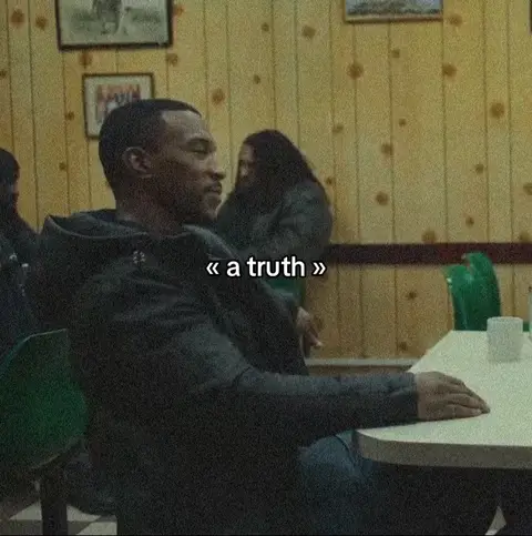 The image captures a scene in a dimly lit diner setting, featuring a man in a dark jacket seated at a table. The man, positioned in the frame's left half, is seen in profile, gazing away from the camera. Behind him, another individual with long hair is partially visible. A text overlay that reads "a truth" is added.