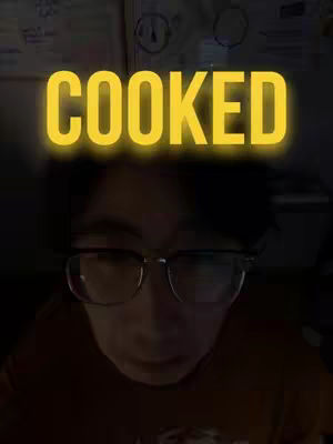 A person in glasses is centered in the frame, staring intently at the camera. Above their head, the word "COOKED" is displayed in a large, glowing yellow font. The background is dark, suggesting a dim environment.