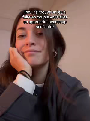 A young woman with long brown hair is featured in a close-up shot with the text overlayed on the top. She is wearing a black jacket over a white top. Her left hand is supporting her chin, and she gazes toward the right, with a slight smile. The background is blurred, suggesting an indoor setting.