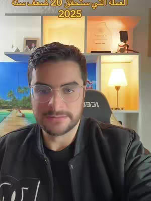 A man wearing glasses and a black jacket is centered in the shot, looking directly at the camera. Behind him, there's a clean, well-lit space with shelves. Above, text announces "The currency that will double in 20 years." In the background are awards, lights, and framed photos, and the number "2025" is also visible.