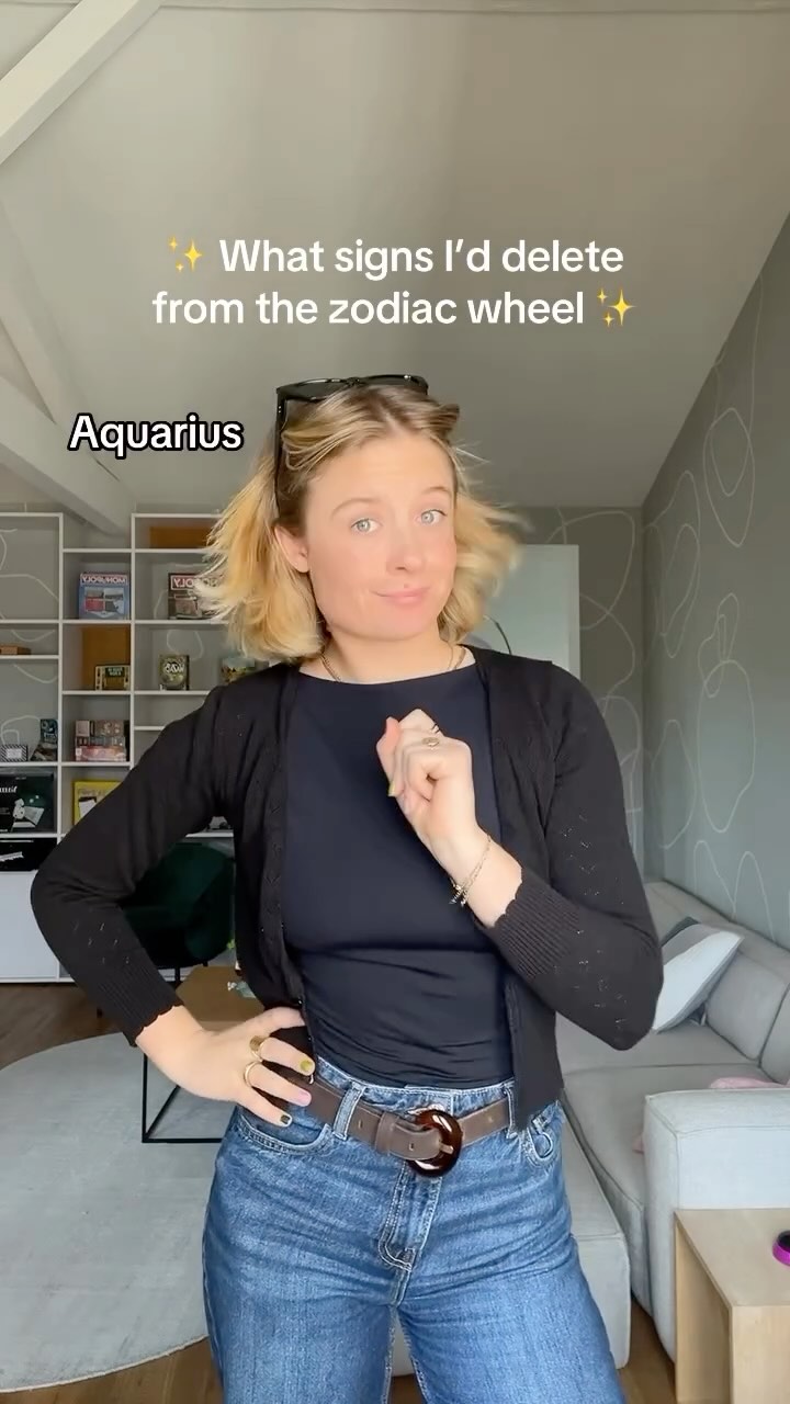 A woman with blonde hair wearing a black top, cardigan, and blue jeans stands in a well-lit room with a neutral-colored background. She's looking at the camera with a slight smirk and raised eyebrows, and a hand raised near her face appearing ready to snap. Text overlays the image.