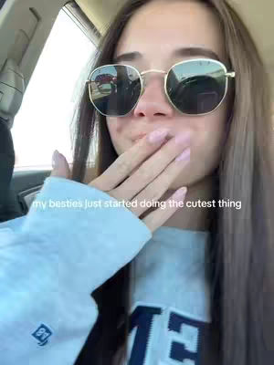 A selfie taken from inside a car, featuring a young woman with sunglasses and a light-colored sweatshirt. She is holding her hand up to her mouth, and text is overlaid on the image.