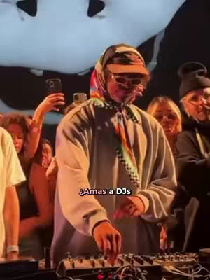 The image shows a DJ in front of a crowd. The DJ is wearing a scarf and hat. Text in a box at the bottom says, "¿Amas a DJs".