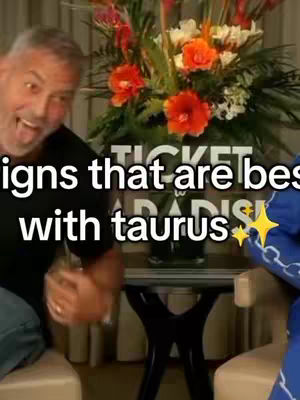 A man smiles with teeth, holding something toward the viewer. Text is overlaid that reads: "signs that are best with taurus" and there's a floral arrangement behind the man and to his right.
