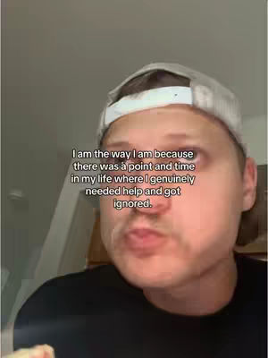 A close-up shot features a man wearing a baseball cap and a black shirt, positioned indoors. Text overlayed on the image reads: 'I am the way I am because there was a point and time in my life where I genuinely needed help and got ignored.' The man has a neutral expression.
