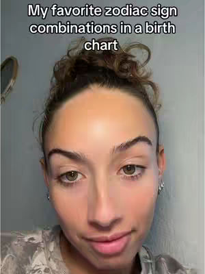 A selfie-style shot featuring a woman from the chest up, centered in the frame. She has light skin, dark hair styled up, brown eyes, and is looking towards the viewer with a slight smile. The background is a plain, pale color. Text overlayed at the top says, 'My favorite zodiac sign combinations in a birth chart'.
