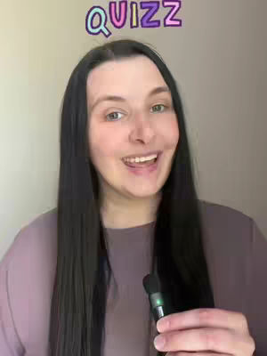 A smiling woman with long dark hair holds a microphone, with a colorful 'QUIZZ' text overlay at the top of her head. She is wearing a mauve shirt and the background is a solid neutral color.