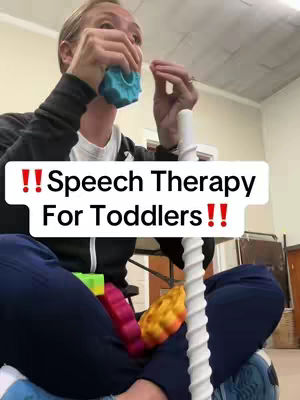A woman wearing a black hoodie and dark blue pants, is sitting cross-legged holding and manipulating blue toy. She seems to be in a work environment. The video has a white text over a white rectangle that emphasizes the main subject of the video.