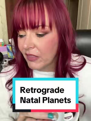 A woman is centered in the frame, shot from the chest up, with light skin, long deep crimson hair, and a white top. Her hair is parted on the side and the bangs are swept to the side. She has makeup on, including eye shadow and lipstick. The phrase "Retrograde Natal Planets" is featured in a box on the screen.