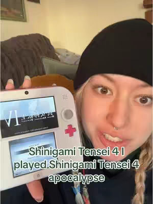 A woman with blonde hair in braids is holding a white 3DS, the screen displays an open game. Text overlay at the bottom reads "Shinigmai Tensei 4 I played Shinigami Tensei 4 apocalypse". She is smiling at the camera with a black beanie.