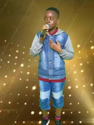 A young person with dark hair and a microphone is featured against a shimmering gold background with scattered bokeh lights. The person is dressed in a layered outfit with a denim jacket, a red undershirt, and blue jeans, striking a pose as though singing, with the right hand over the chest.