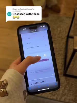 A person's hand holding and operating a smartphone. The phone displays a video editing interface with a colorful waveform and several menu options.