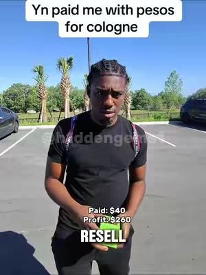 A man stands in a parking area under a bright sky. He is wearing a black t-shirt and holding a small green item while facing the camera. Text overlays indicate a financial transaction.