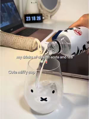 A person is pouring a clear liquid from a bottle into a clear glass with a Miffy face on it. The time is shown on a digital clock as 23:18:26.