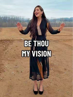 A woman with long dark hair stands outdoors with her arms outstretched. She is wearing a dark, long, flowing dress with a lighter underskirt, and black shoes. Her face shows a big smile and open mouth, and in front of her is a text overlay.
