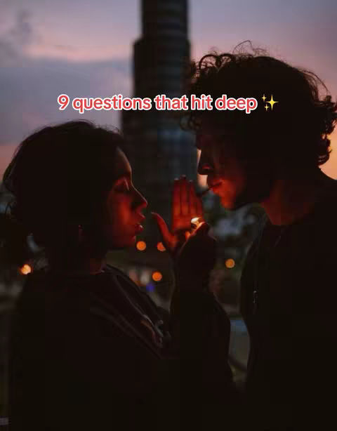 A silhouette of a couple facing each other at twilight. The woman holds what seems to be a lighter near the man's face. The background consists of an out-of-focus cityscape under a colorful sky.