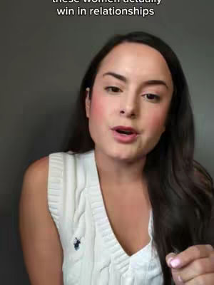 A woman with long dark hair, wearing a white sweater vest, is looking at the camera and speaking. Text overlay reads "these women actually win in relationships". The background is a solid gray.