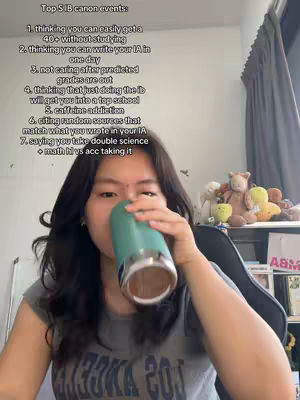 A young woman is seen from the chest up, seated inside a room. She is holding a teal-colored drink container up to her face, appearing to take a drink. Prominently displayed on the screen is a list of seven points titled "Top 5 IB canon events." Behind her, a partially visible white shelf hosts a collection of stuffed animals and other decorations, hinting at a casual domestic setting and adding context to the shot.