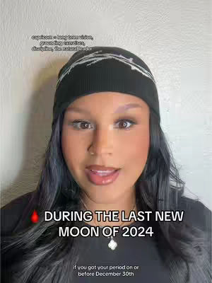 A woman with long, dark hair wearing a black beanie and a black top has an overlay of text. She is looking at the camera and talking.
