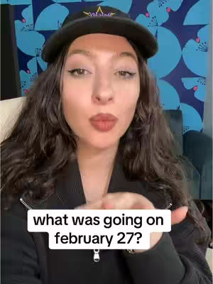 A woman with long dark hair wearing a black cap and jacket is blowing a kiss towards the camera, with a blue floral pattern in the background. A white text box with black text appears at the bottom of the screen.