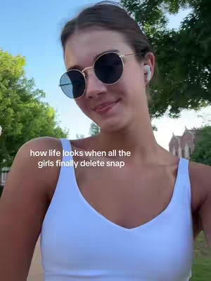 A young woman with brown hair and sunglasses poses outdoors. She wears a white tank top, and the background shows a green environment under a blue sky. Text overlayed on the image adds context.