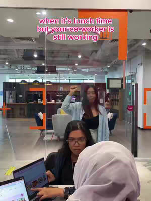 The cover image shows three women in an office setting. The foreground features two women sitting at a desk with laptops, while a third woman stands in the background, raising her fist. A text overlay says, "when it's lunch time but your co-worker is still working."