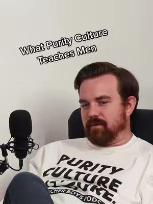 A man with a beard sits in front of a microphone, wearing a white t-shirt with a graphic on it. Text overlays the top of the image.