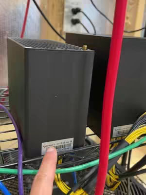 The cover image shows a close-up shot of two black crypto mining machines on a metal rack. The machines are rectangular, with visible power cords and wiring. A finger is pointing to a label on the front of one of the machines. The background includes white electrical outlets and a wooden wall.