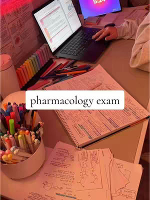 A well-lit study space featuring a laptop displaying notes, surrounded by open books, handwritten notes, and colorful markers, suggesting an exam study session.