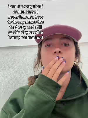 A young woman with fair skin is shown from the chest up, covering her mouth with her hand. She wears a green hoodie and a maroon baseball cap. Text is overlaid on the image.