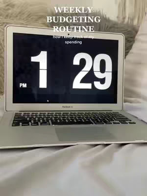 An open laptop displays a digital clock set to 1:29 PM. Text overlays describe the video's subject: a weekly budgeting routine.