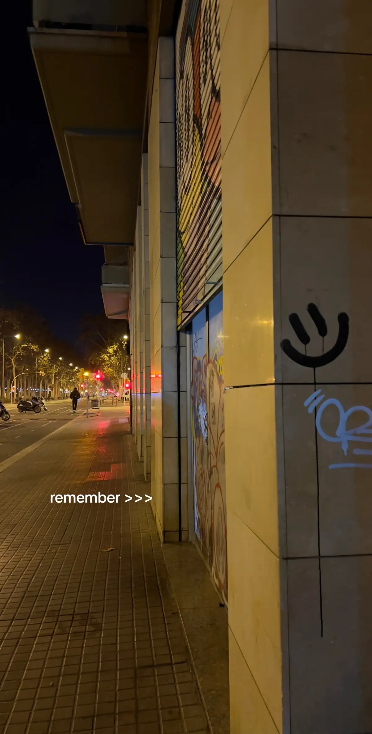 An urban night scene featuring a well-lit sidewalk and building facade. The sidewalk, made of rectangular tiles, stretches towards the background, with a road and streetlights on the left. A building with a textured facade stands on the right, and a smiley face graffiti marks a section of the wall. The hook text is placed on the sidewalk.