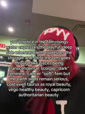 A selfie-style video cover shows a person wearing a red beanie and a black top. The person is in front of what looks like a food store. Text overlayed reads: 'you'll notice in the fem risings water expresses the playful, deep side whereas earth expresses the struggle and strife the fem goes through like pisces being transcendental, scorpio "dark" feminine, cancer "soft" fem but the earth signs remain serious, cold even taurus as royal beauty, virgo healthy beauty, capricorn authoritarian beauty'.