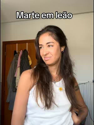 The cover image features a woman with long, dark hair in a white tank top, looking slightly to her left. The background is a simple room with a door and some clothing items hanging in the background. Text overlayed on top reads "Marte em leão".