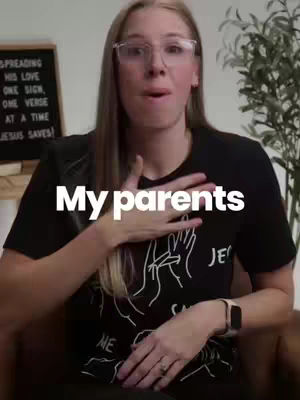 A woman with long blonde hair and glasses is the focus, looking directly at the camera with a surprised or open-mouthed expression. She is wearing a dark t-shirt featuring white graphics of hands in ASL. Overlaid in a bold white font is the text 'My parents'. In the background, a framed message board displays text, and a green plant is also visible. The composition is well-lit.